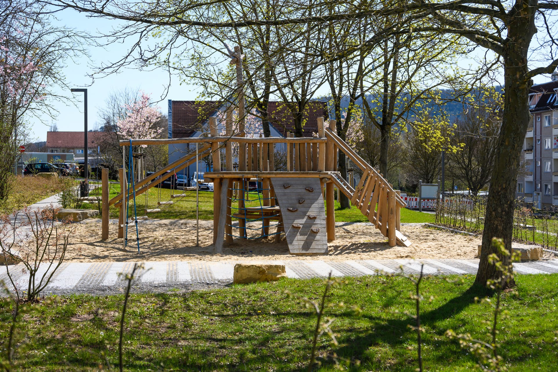 Spielplatz mit Klettergerüst und Rutsche im Mietergarten der KOWO Heiligenstadt, umgeben von Bäumen und Grünflächen.