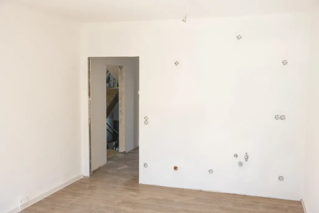 Leerer, frisch verputzter Raum einer Neubauwohnung auf den Liethen mit Anschlüssen an der Wand und Blick ins Treppenhaus