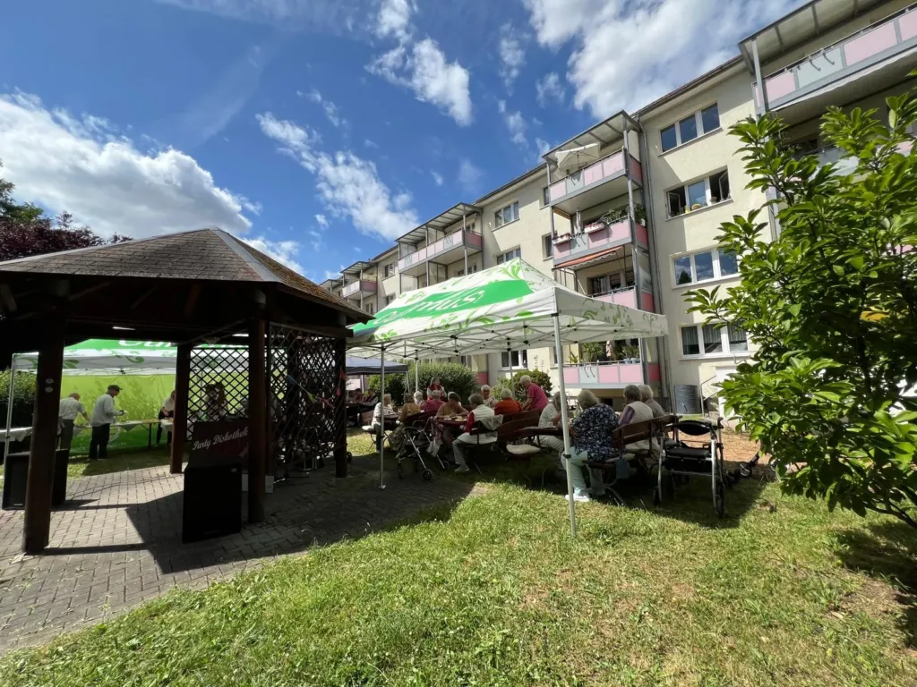 Bewohner der KOWO Obereichsfeld feiern das Curamus Sommerfest im Garten der Wohnanlage unter Pavillons und Sonnensegeln.