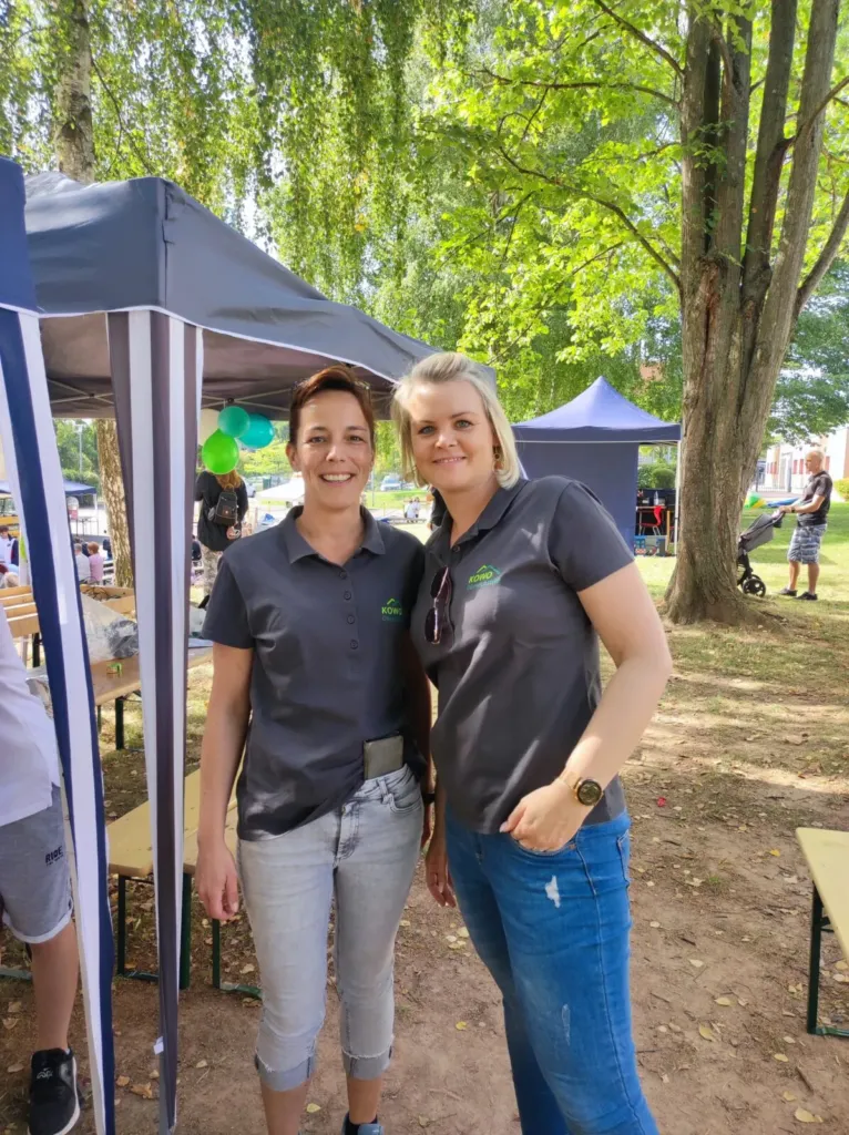 Zwei KOWO-Mitarbeiterinnen in Firmenpolo beim Stadtteilfest Liethen 2023 vor einem Pavillonzelt im Grünen