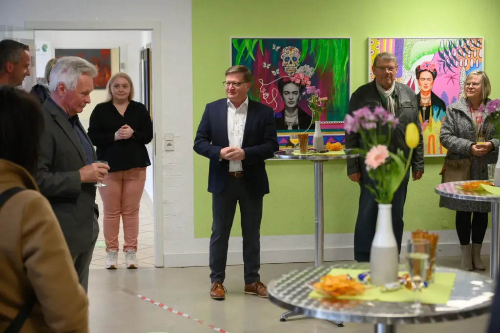 Gäste bei der Ausstellungseröffnung im Quartier 44, im Hintergrund bunte Frida-Kahlo-Gemälde an der Wand.