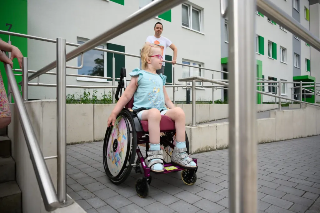 Mädchen im Rollstuhl nutzt barrierefreie Rampe an KOWO-Wohnanlage im Obereichsfeld, Vater begleitet sie.